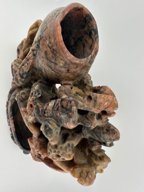 fig 3. A Qing dynasty Chinese soapstone carving depicting a small vase, a shallow brush washer basin, and carved birds among naturalistic floral motifs in mottled red, grey, and cream stone.