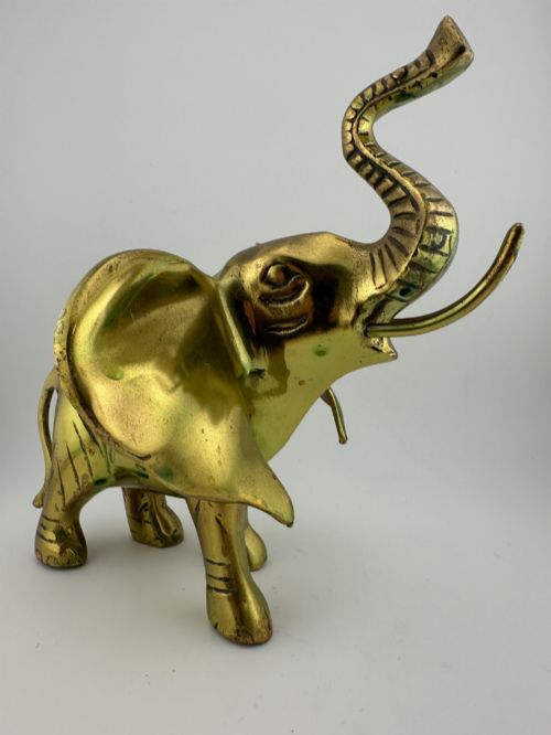 fig 1. A solid cast brass elephant sculpture with an elevated raised trunk, detailed engraving along the body, and a polished gold finish.