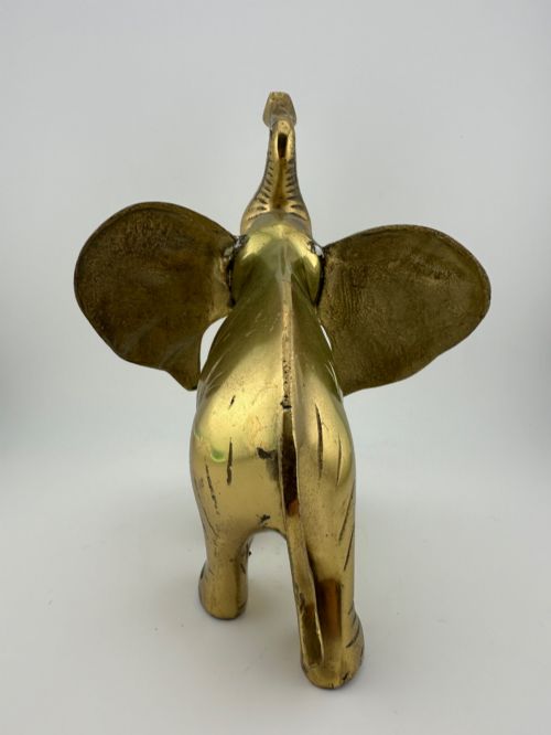 fig 3. A solid cast brass elephant sculpture with an elevated raised trunk, detailed engraving along the body, and a polished gold finish.