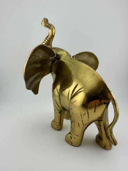 fig 4. A solid cast brass elephant sculpture with an elevated raised trunk, detailed engraving along the body, and a polished gold finish.