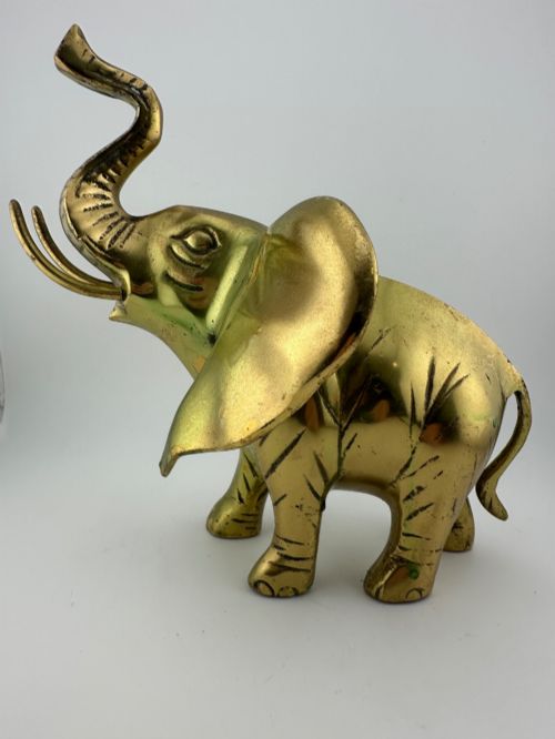 fig 5. A solid cast brass elephant sculpture with an elevated raised trunk, detailed engraving along the body, and a polished gold finish.