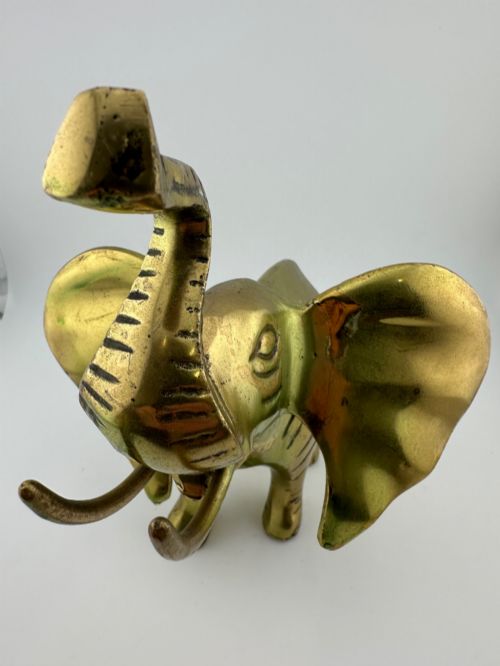fig 8. A solid cast brass elephant sculpture with an elevated raised trunk, detailed engraving along the body, and a polished gold finish.
