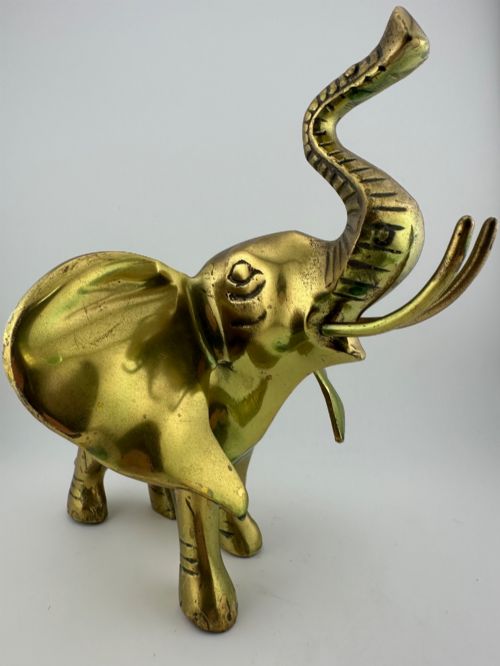 fig 9. A solid cast brass elephant sculpture with an elevated raised trunk, detailed engraving along the body, and a polished gold finish.