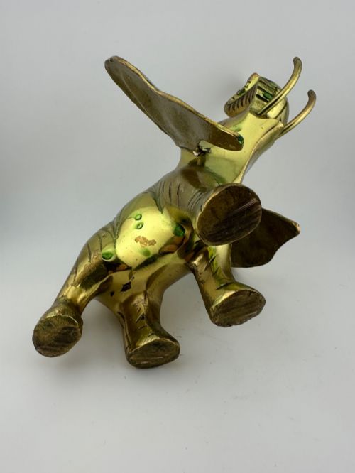 fig 10. A solid cast brass elephant sculpture with an elevated raised trunk, detailed engraving along the body, and a polished gold finish.