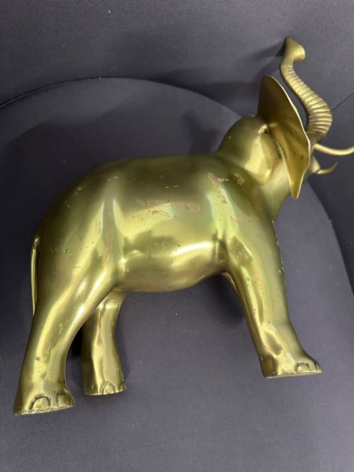 fig 7. A vintage cast brass elephant sculpture standing with its trunk raised high.