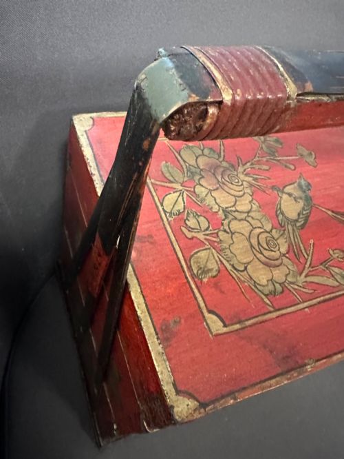 fig 2. A three-tiered Chinese red lacquer wedding basket featuring hand-painted gold floral motifs and a black wooden carrying handle.