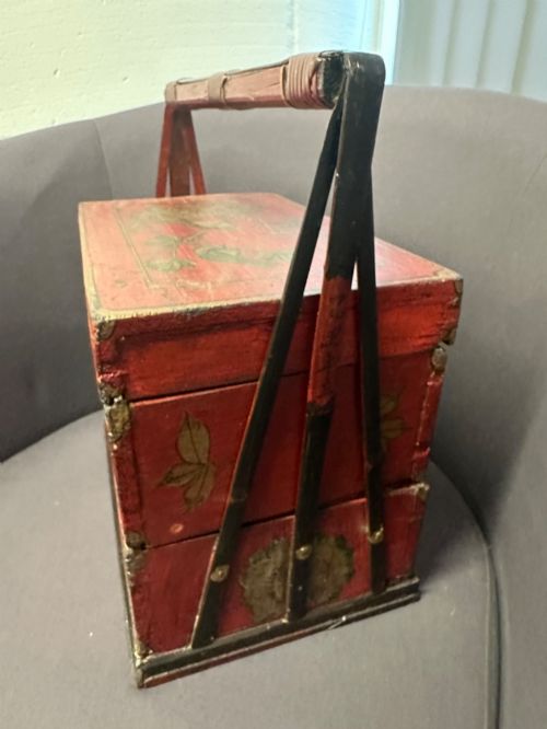fig 3. A three-tiered Chinese red lacquer wedding basket featuring hand-painted gold floral motifs and a black wooden carrying handle.