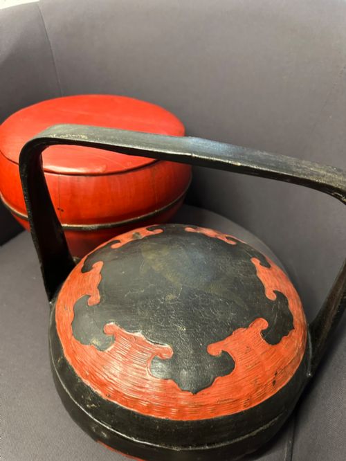 fig 2. A traditional Chinese red and black lacquered rice basket featuring a high arched handle and painted decorative motifs on the lid.