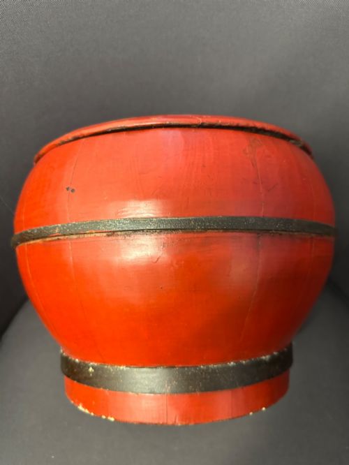 fig 3. A traditional Chinese red and black lacquered rice basket featuring a high arched handle and painted decorative motifs on the lid.