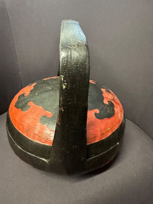 fig 4. A traditional Chinese red and black lacquered rice basket featuring a high arched handle and painted decorative motifs on the lid.