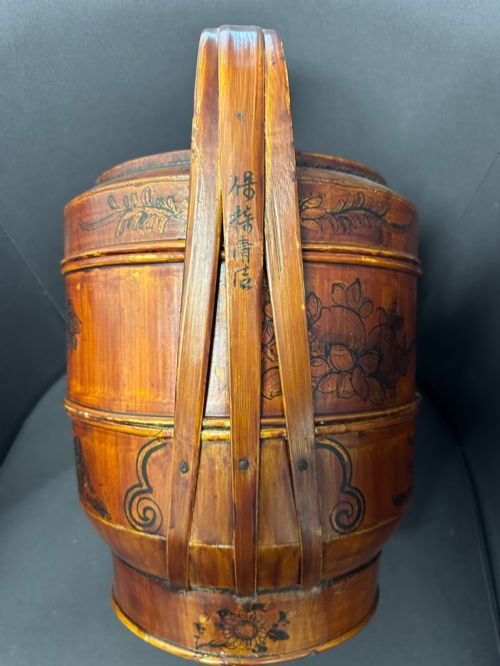 fig 2. A late Qing Dynasty tiered Chinese food basket crafted from warm amber bamboo and wood, hand-painted with black line illustrations of a child on the lid and floral motifs around the body.