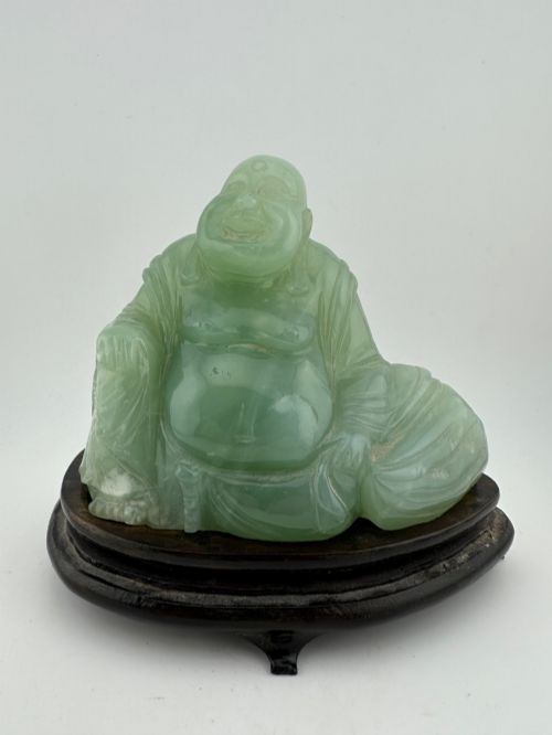 fig 1. A hand-carved light green jadeite sculpture depicting a seated Laughing Buddha resting on a dark wooden fitted base.