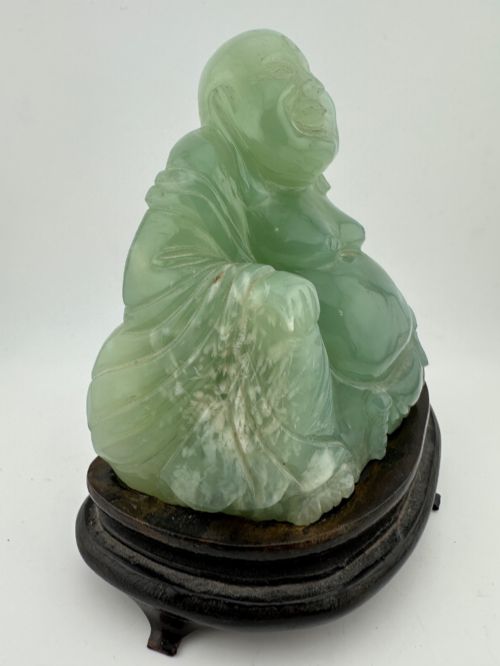 fig 3. A hand-carved light green jadeite sculpture depicting a seated Laughing Buddha resting on a dark wooden fitted base.