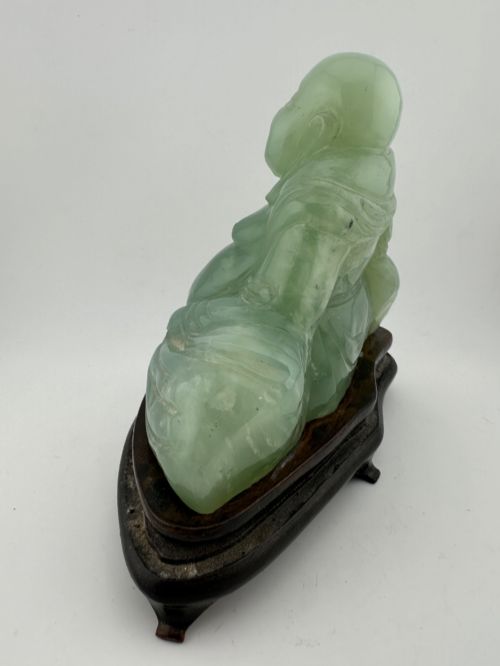 fig 5. A hand-carved light green jadeite sculpture depicting a seated Laughing Buddha resting on a dark wooden fitted base.