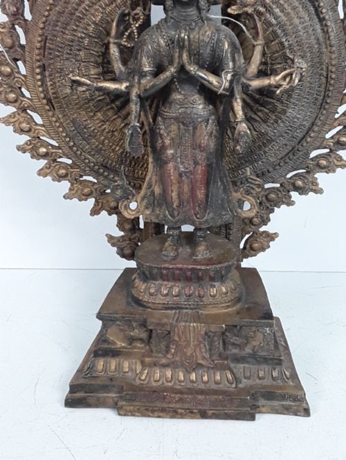 fig 2. A dark bronze Tibetan sculpture depicting the eleven-headed deity Avalokiteshvara standing on a tiered lotus pedestal against an ornate halo.