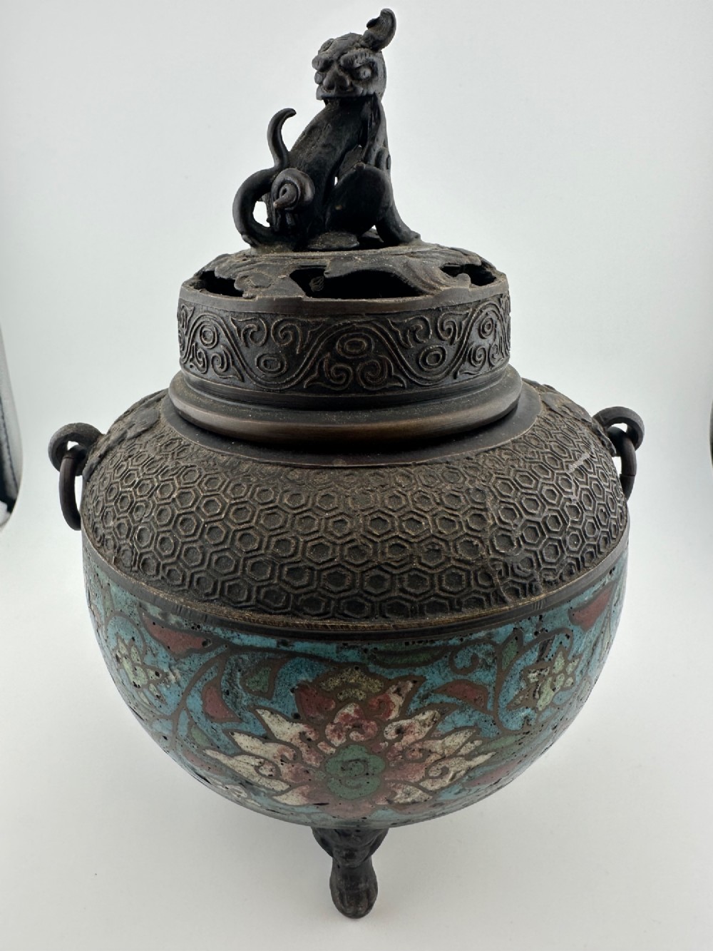 A 19th-century Chinese bronze tripod censer featuring polychrome cloisonne enamel floral motifs, side loop handles, and a lid topped with a Qilin finial. View II