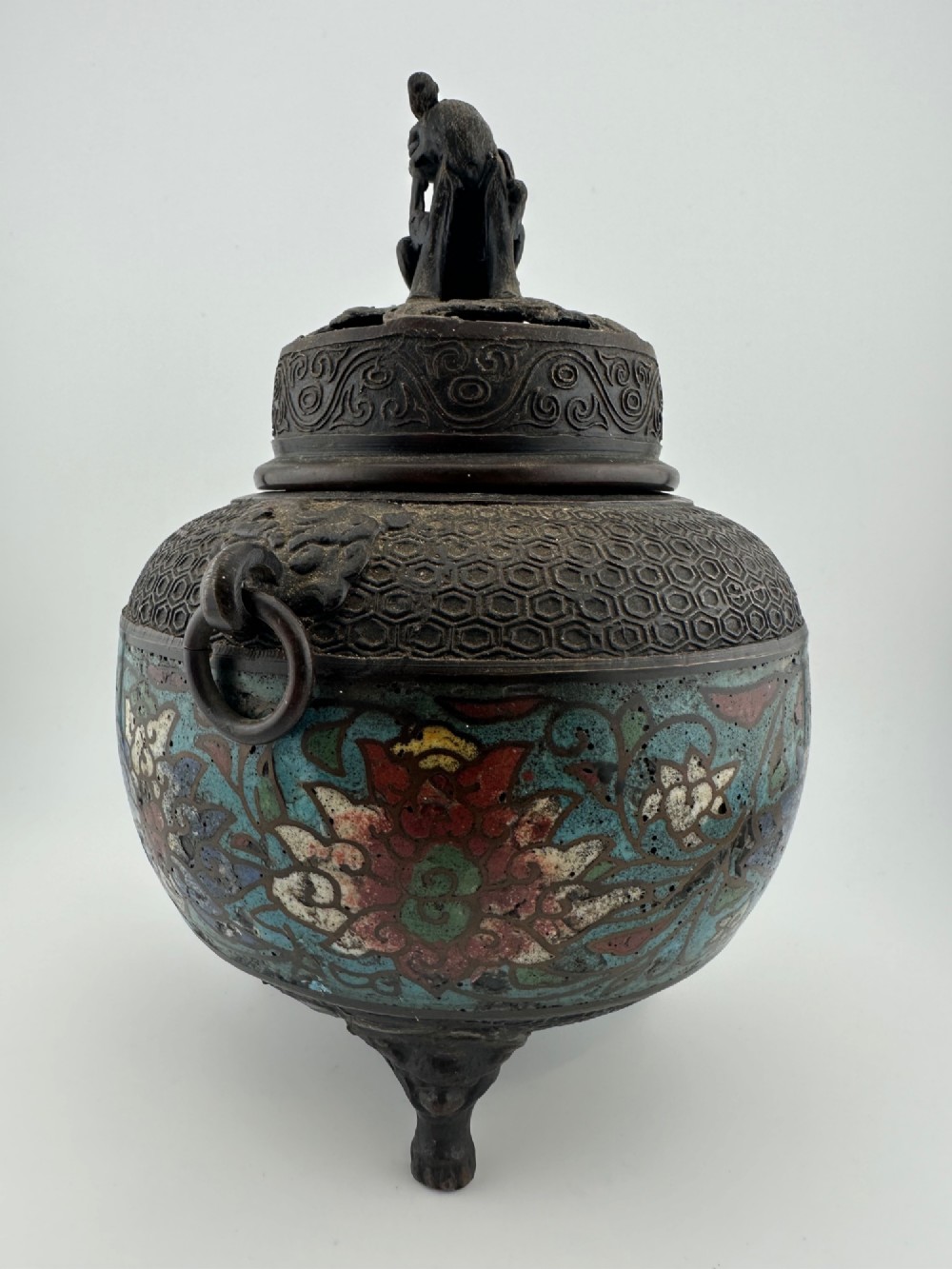 A 19th-century Chinese bronze tripod censer featuring polychrome cloisonne enamel floral motifs, side loop handles, and a lid topped with a Qilin finial. View V
