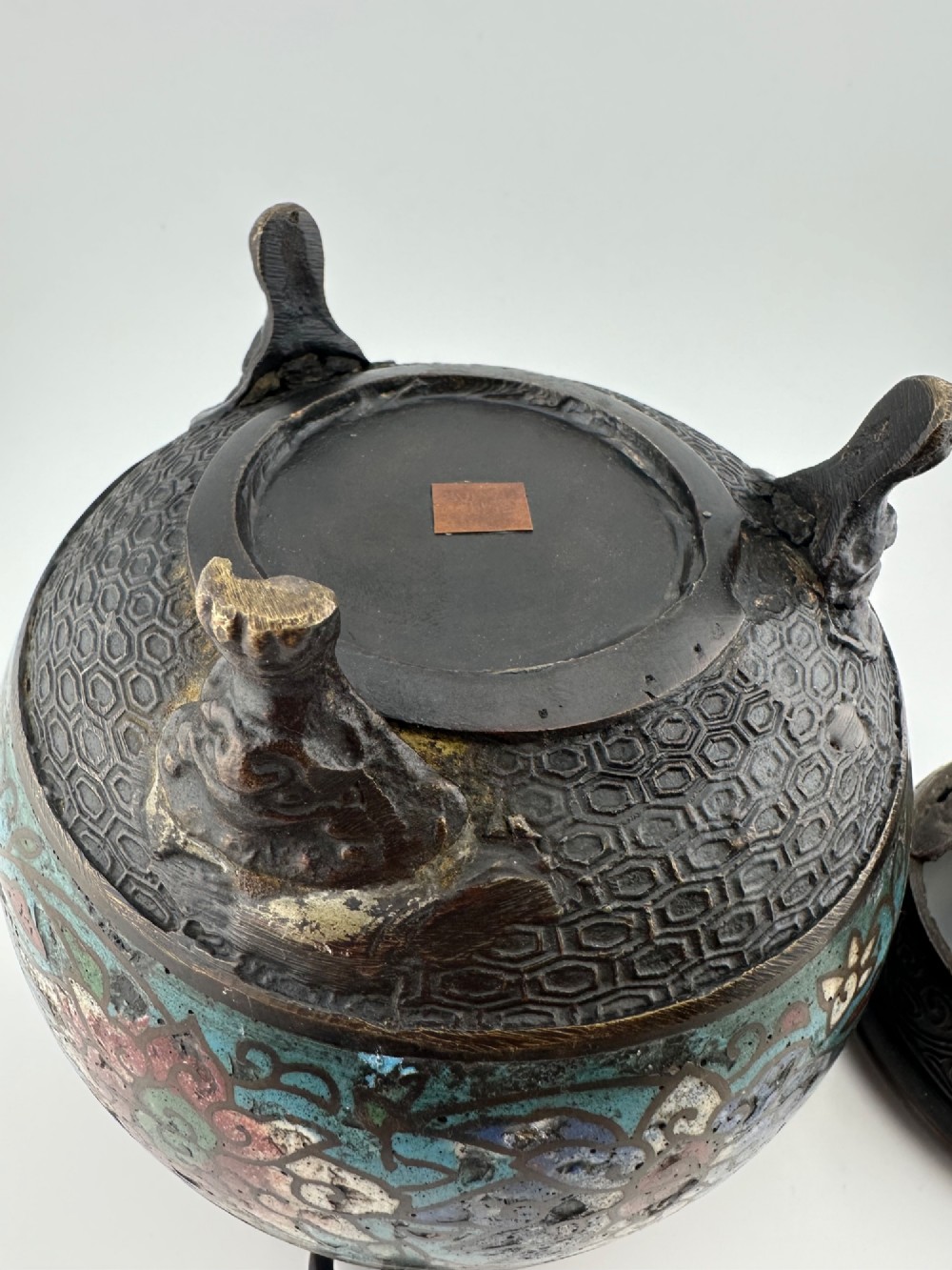 A 19th-century Chinese bronze tripod censer featuring polychrome cloisonne enamel floral motifs, side loop handles, and a lid topped with a Qilin finial. View X