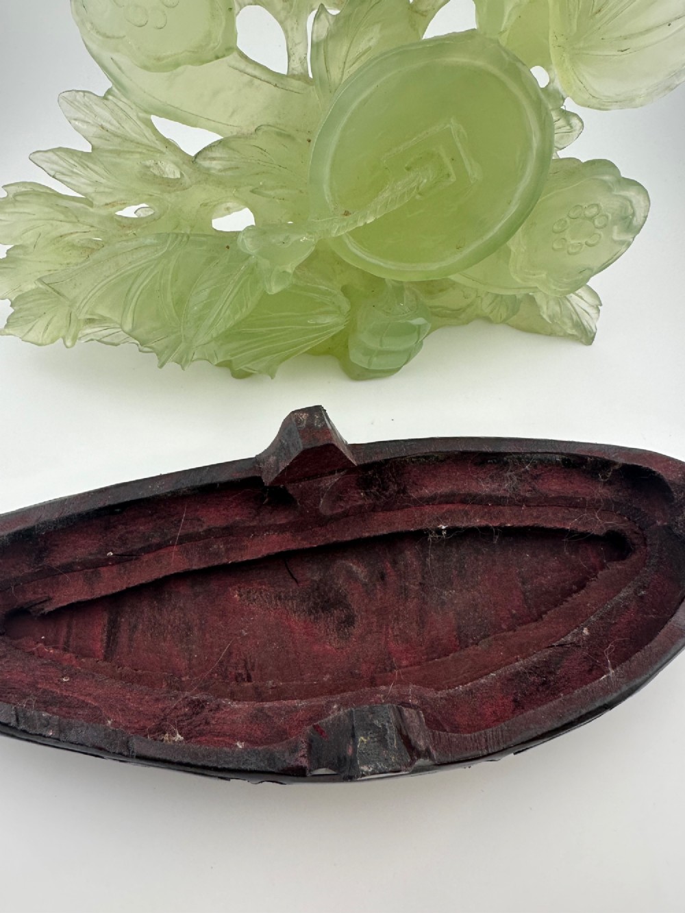 A carved pale green Xiuyan jade sculpture depicting a lotus flower, foliage, and a central cash coin, displayed on a dark carved wooden stand. View XII