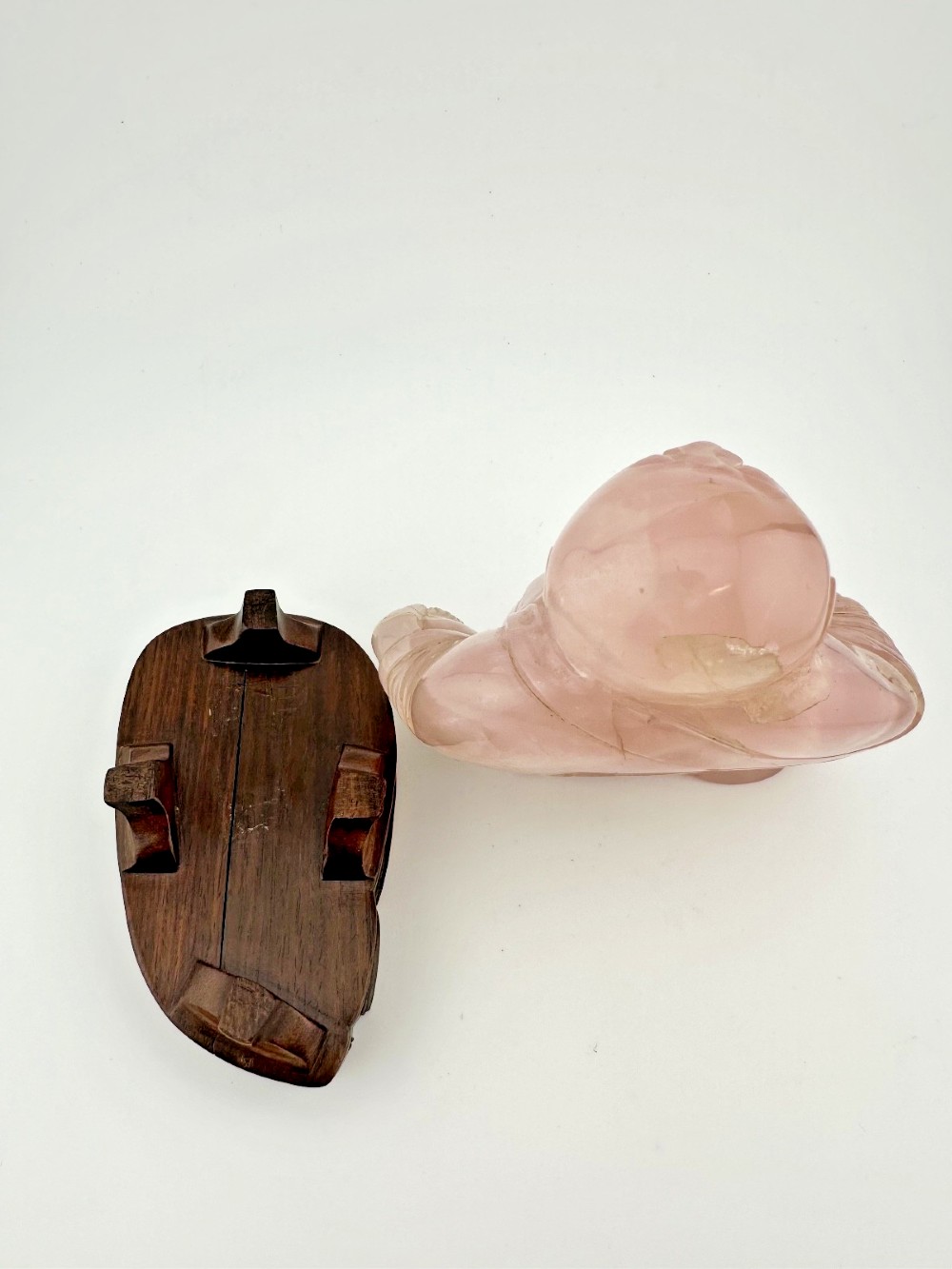 A hand-carved pink rose quartz figure of a seated Laughing Buddha resting upon a custom dark wood stand. View V