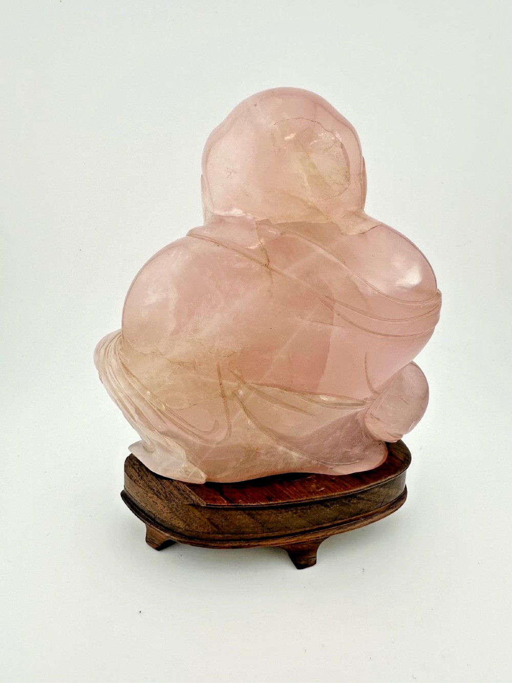 A hand-carved pink rose quartz figure of a seated Laughing Buddha resting upon a custom dark wood stand. View IX