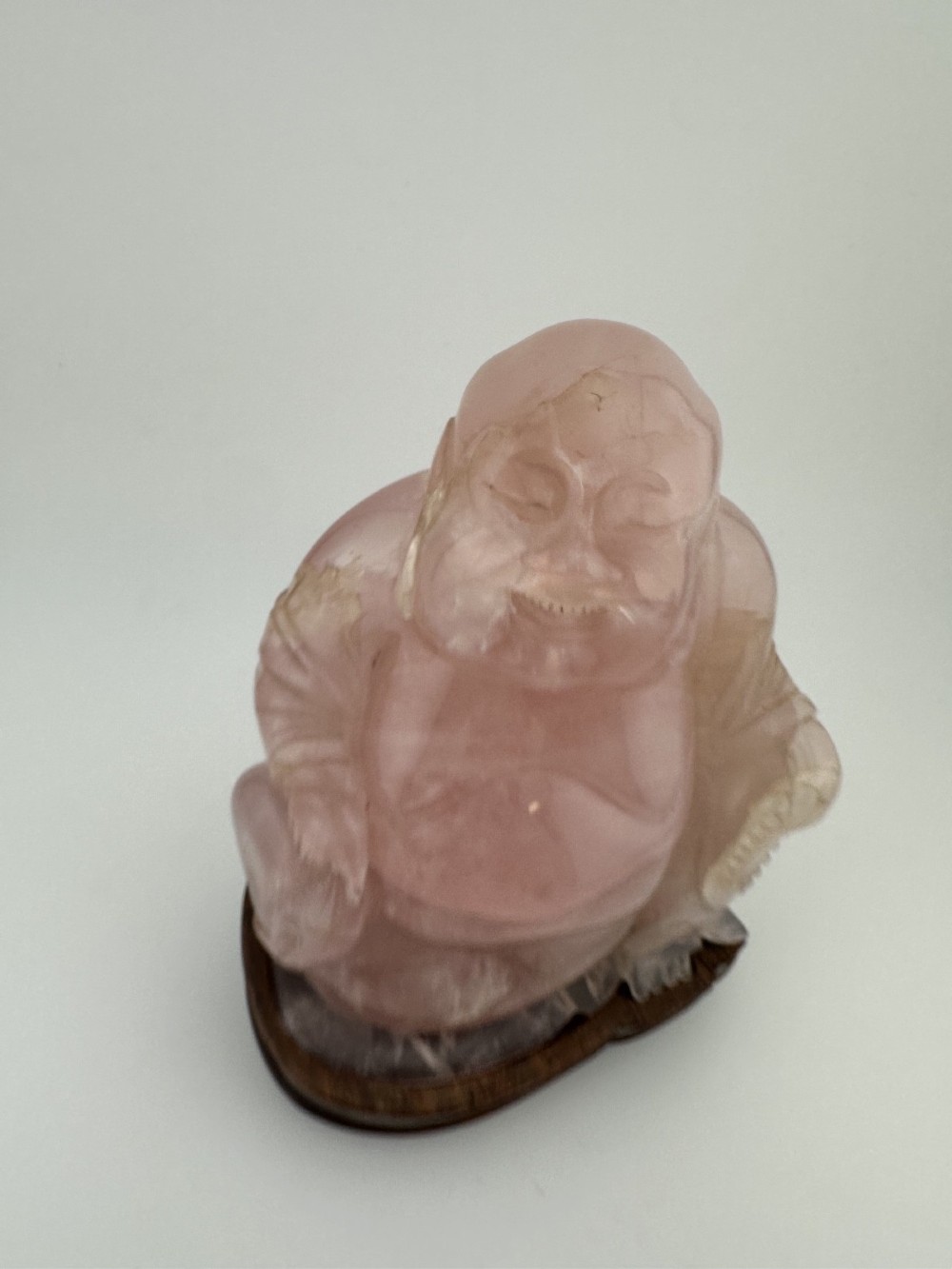 A hand-carved pink rose quartz figure of a seated Laughing Buddha resting upon a custom dark wood stand. View X
