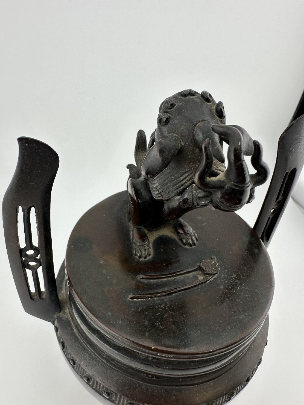 A dark patinated bronze tripod censer featuring raised loop handles, a decorative meander border, and a fitted lid with a standing Qilin finial. View III
