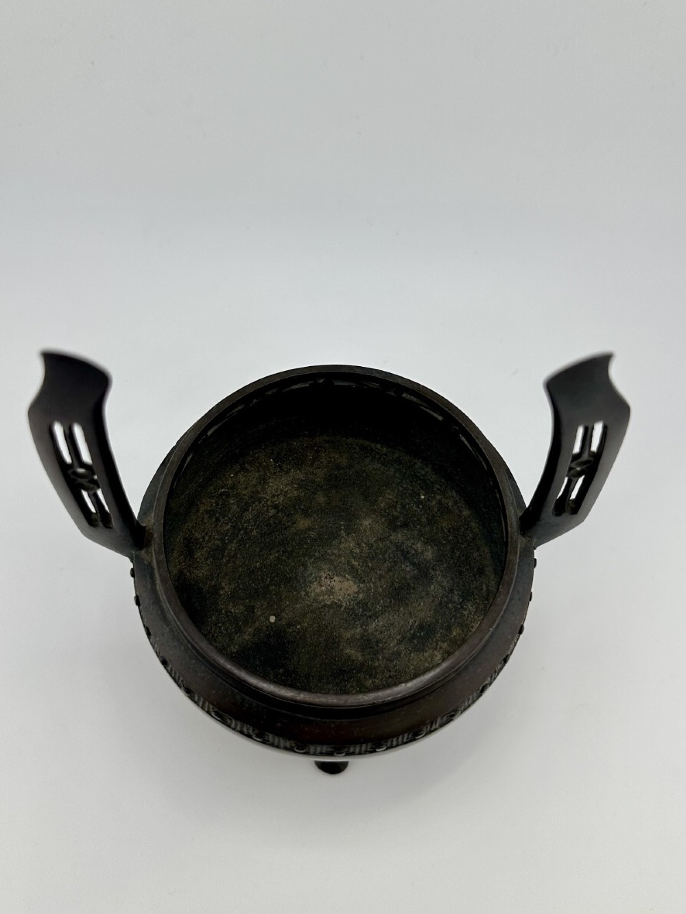 A dark patinated bronze tripod censer featuring raised loop handles, a decorative meander border, and a fitted lid with a standing Qilin finial. View VII
