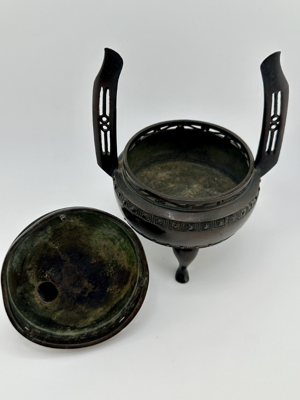 A dark patinated bronze tripod censer featuring raised loop handles, a decorative meander border, and a fitted lid with a standing Qilin finial. View IX