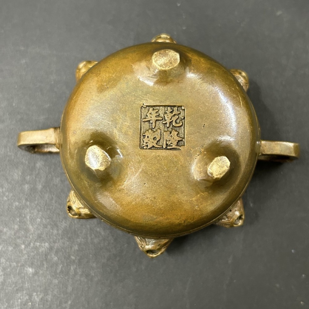 A pair of patinated bronze tripod censers featuring sculpted dragon finials on the lids, side handles, and relief mask carvings around the circular bodies. View V