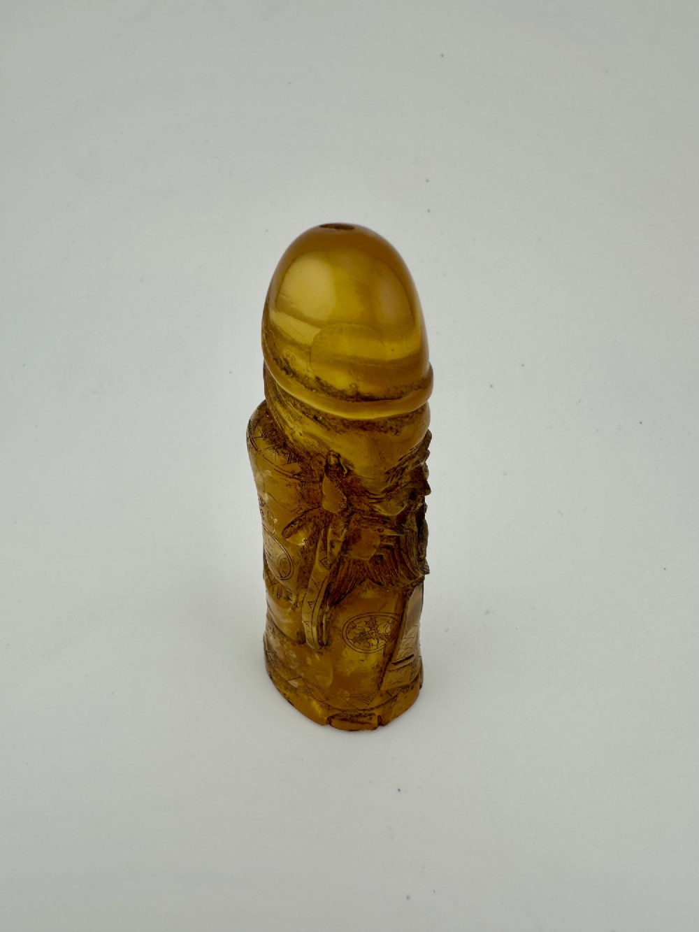 A hand-carved honey amber pendant depicting the Chinese deity Shoulao with incised robe detailing and a high domed head. View VI
