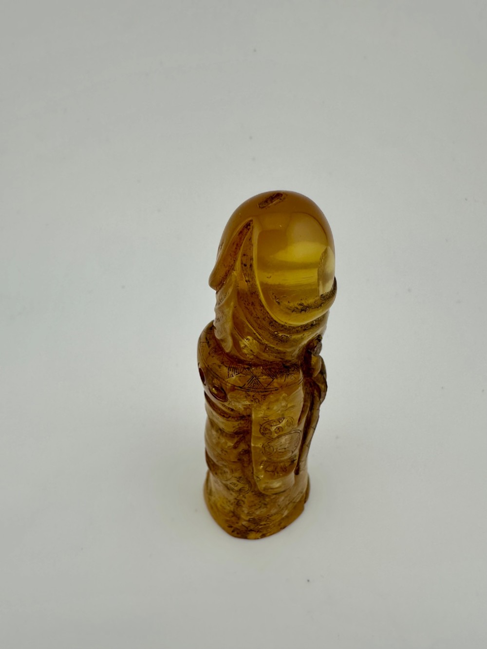 A hand-carved honey amber pendant depicting the Chinese deity Shoulao with incised robe detailing and a high domed head. View VII