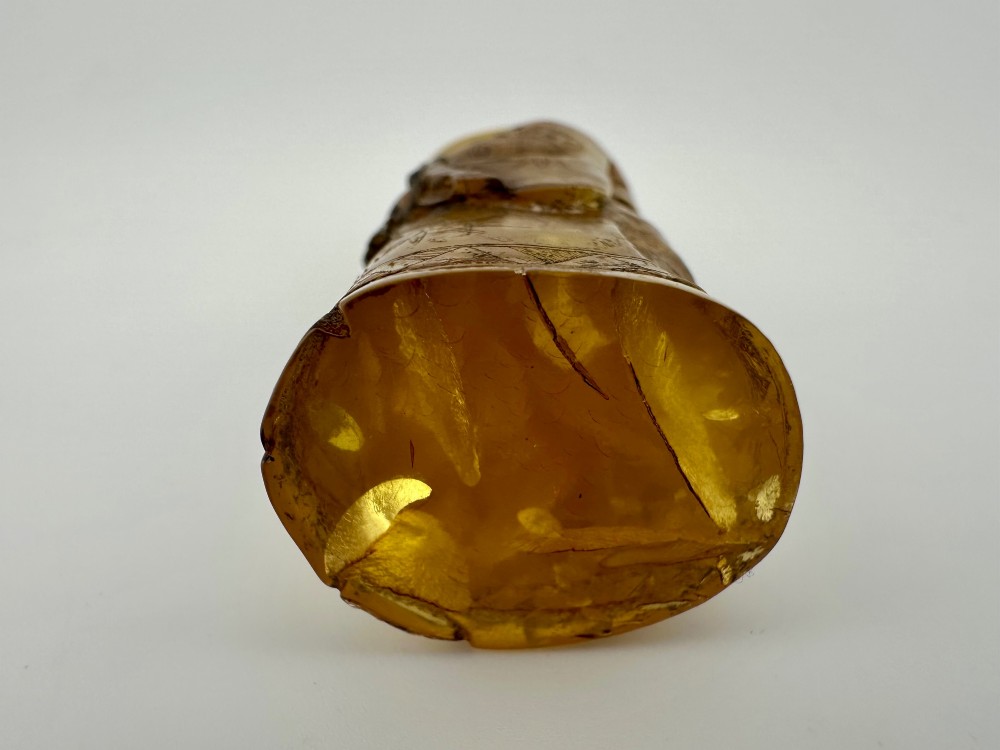 A hand-carved honey amber pendant depicting the Chinese deity Shoulao with incised robe detailing and a high domed head. View IX