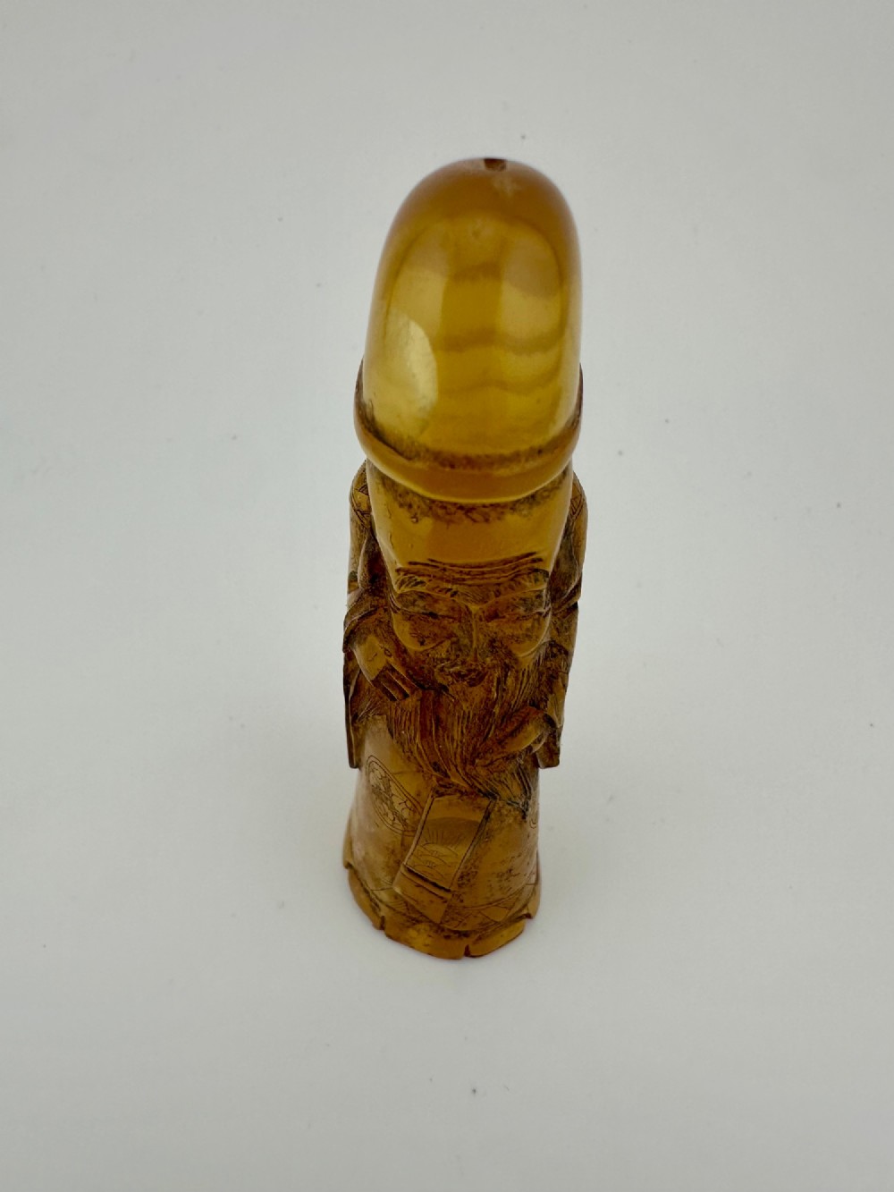 A hand-carved honey amber pendant depicting the Chinese deity Shoulao with incised robe detailing and a high domed head. View X