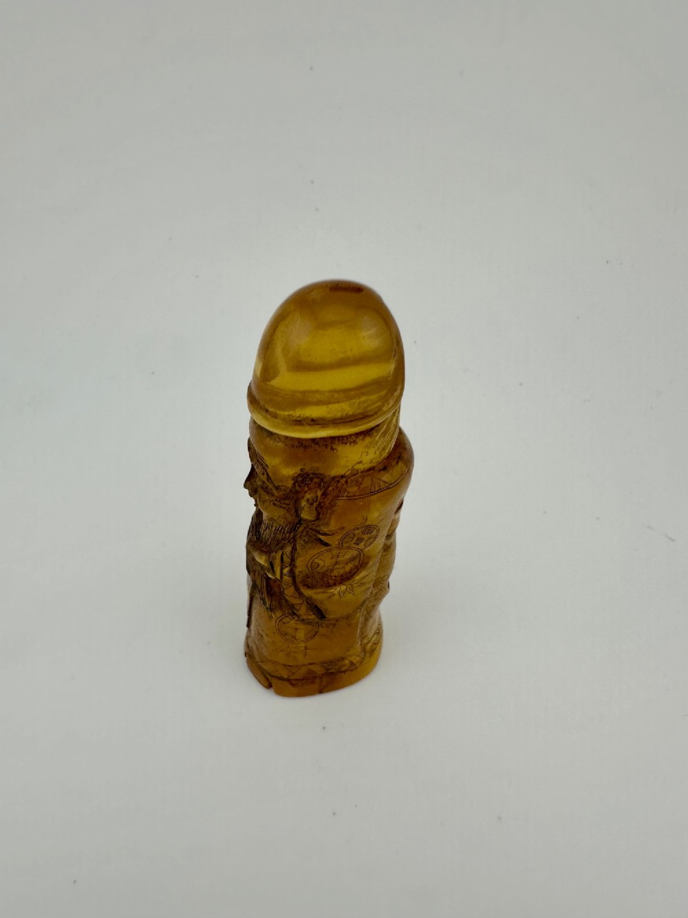 A hand-carved honey amber pendant depicting the Chinese deity Shoulao with incised robe detailing and a high domed head. View XII