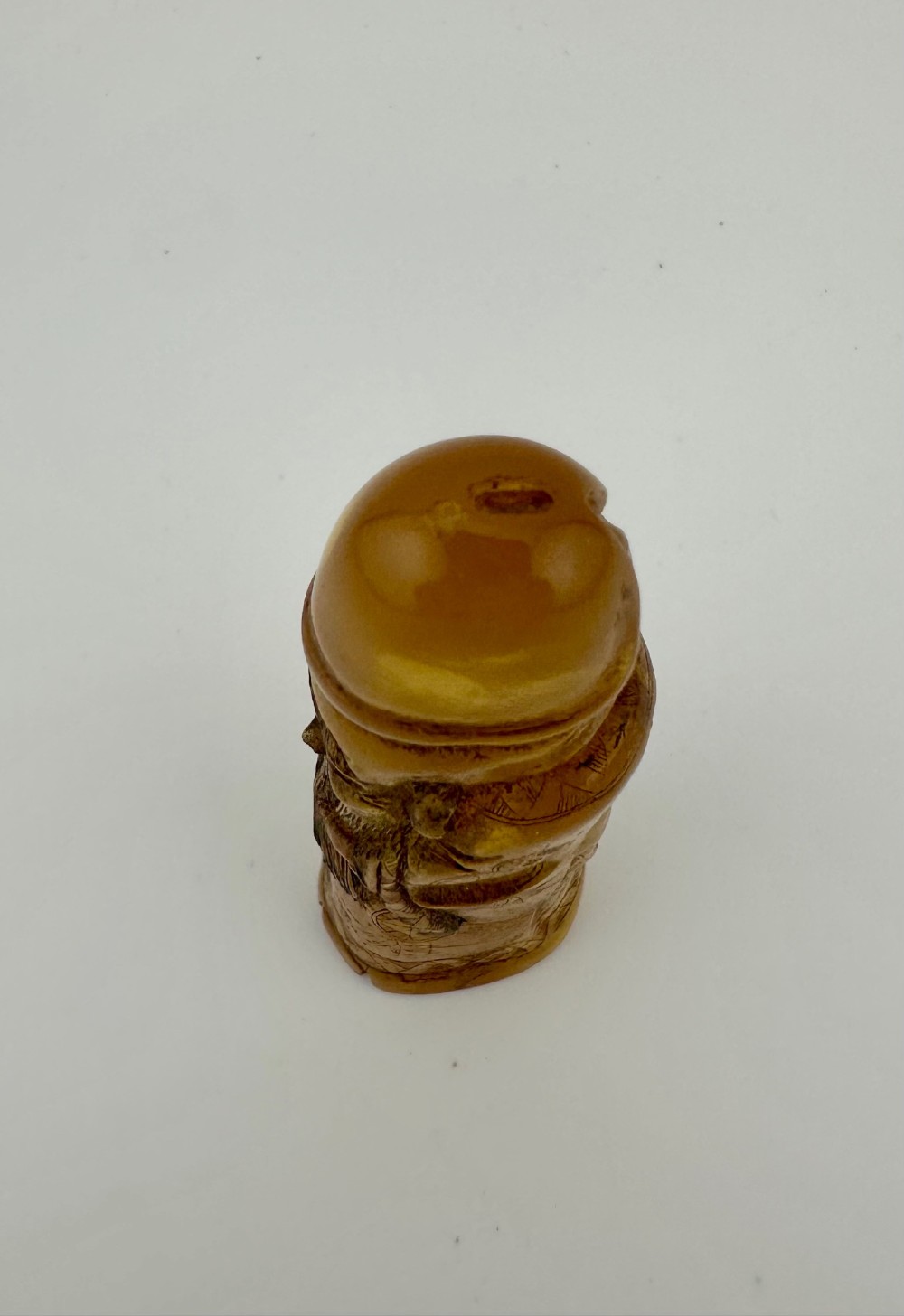 A hand-carved honey amber pendant depicting the Chinese deity Shoulao with incised robe detailing and a high domed head. View XIII