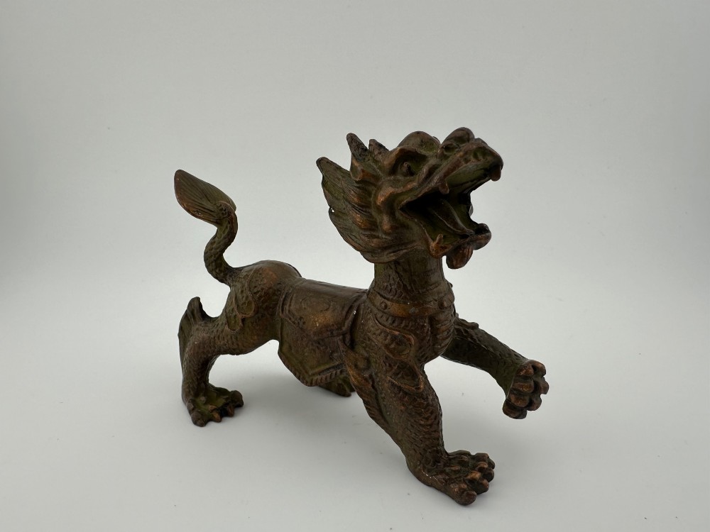 A small patinated dark brown bronze figure of a Chinese mythical beast, standing on four legs with an open mouth and raised tail.