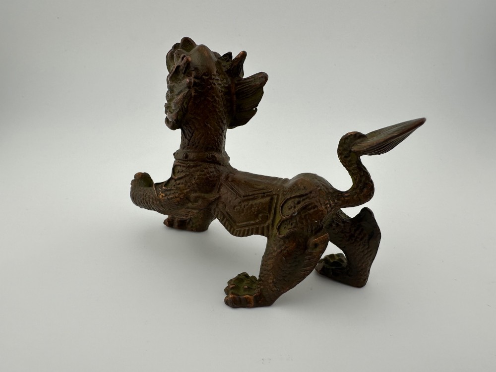 A small patinated dark brown bronze figure of a Chinese mythical beast, standing on four legs with an open mouth and raised tail. View IX