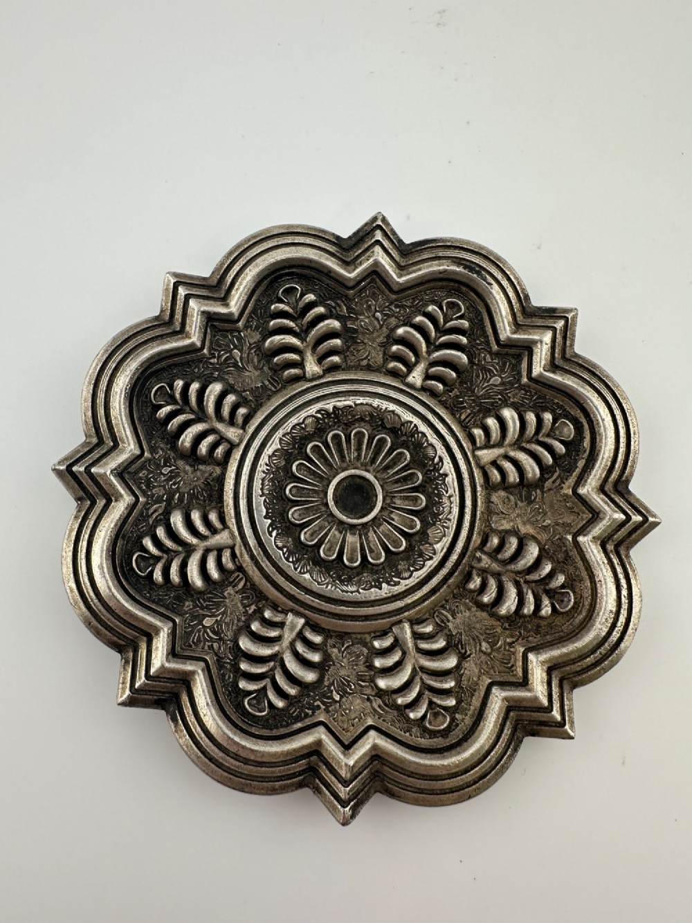 A lobed Chinese white metal dish with raised relief repousse lotus foliage and a central floral motif. View II