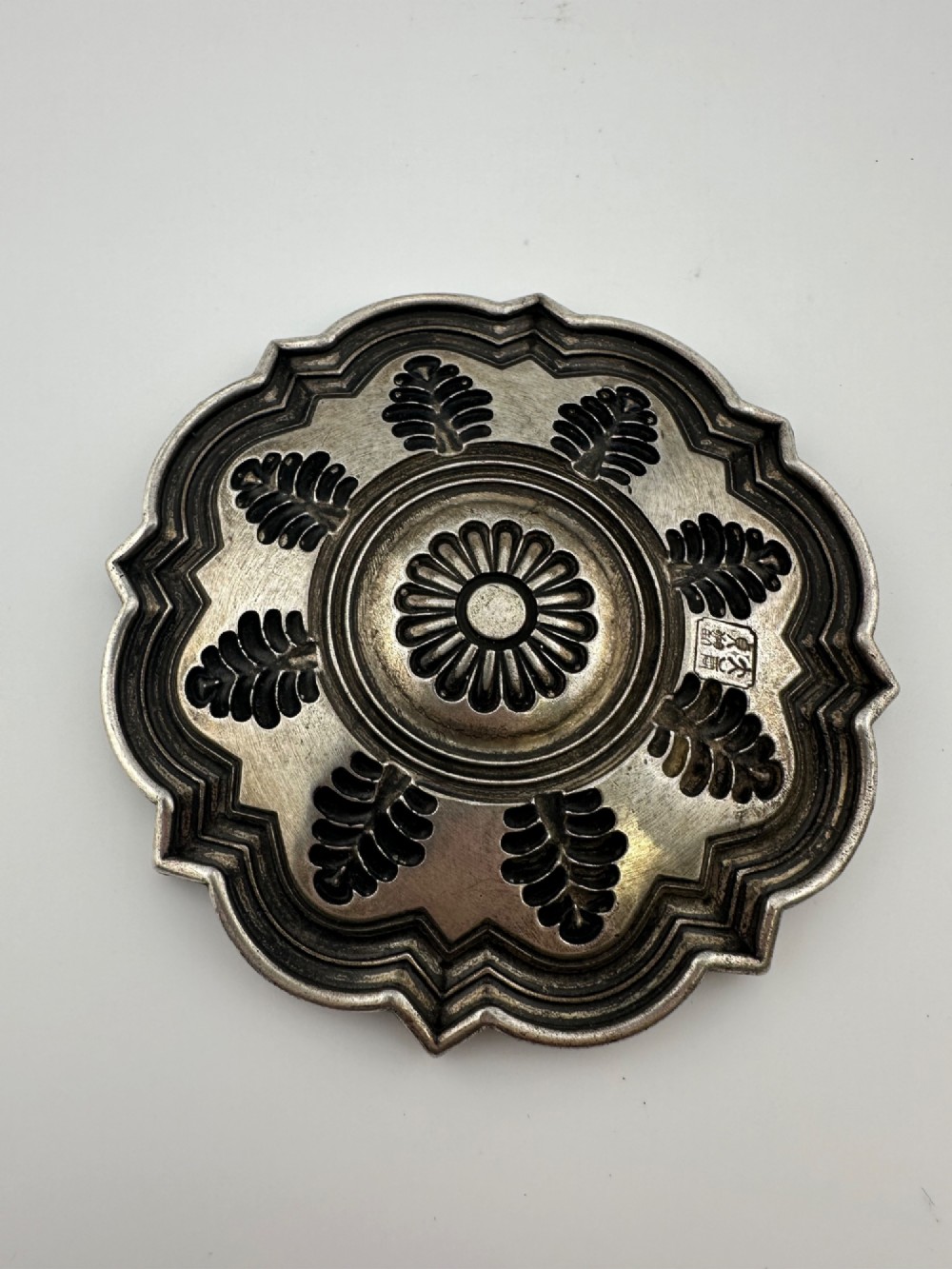 A lobed Chinese white metal dish with raised relief repousse lotus foliage and a central floral motif. View V