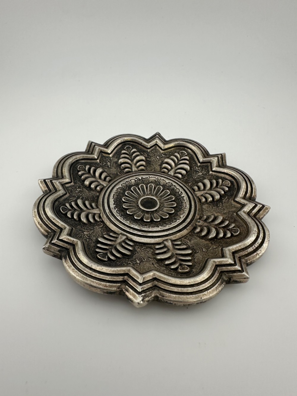 A lobed Chinese white metal dish with raised relief repousse lotus foliage and a central floral motif. View VII