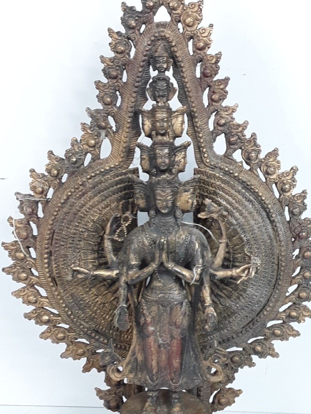 A dark bronze Tibetan sculpture depicting eleven-headed Avalokiteshvara with radiating arms set against a halo mandorla on a lotus pedestal. View II
