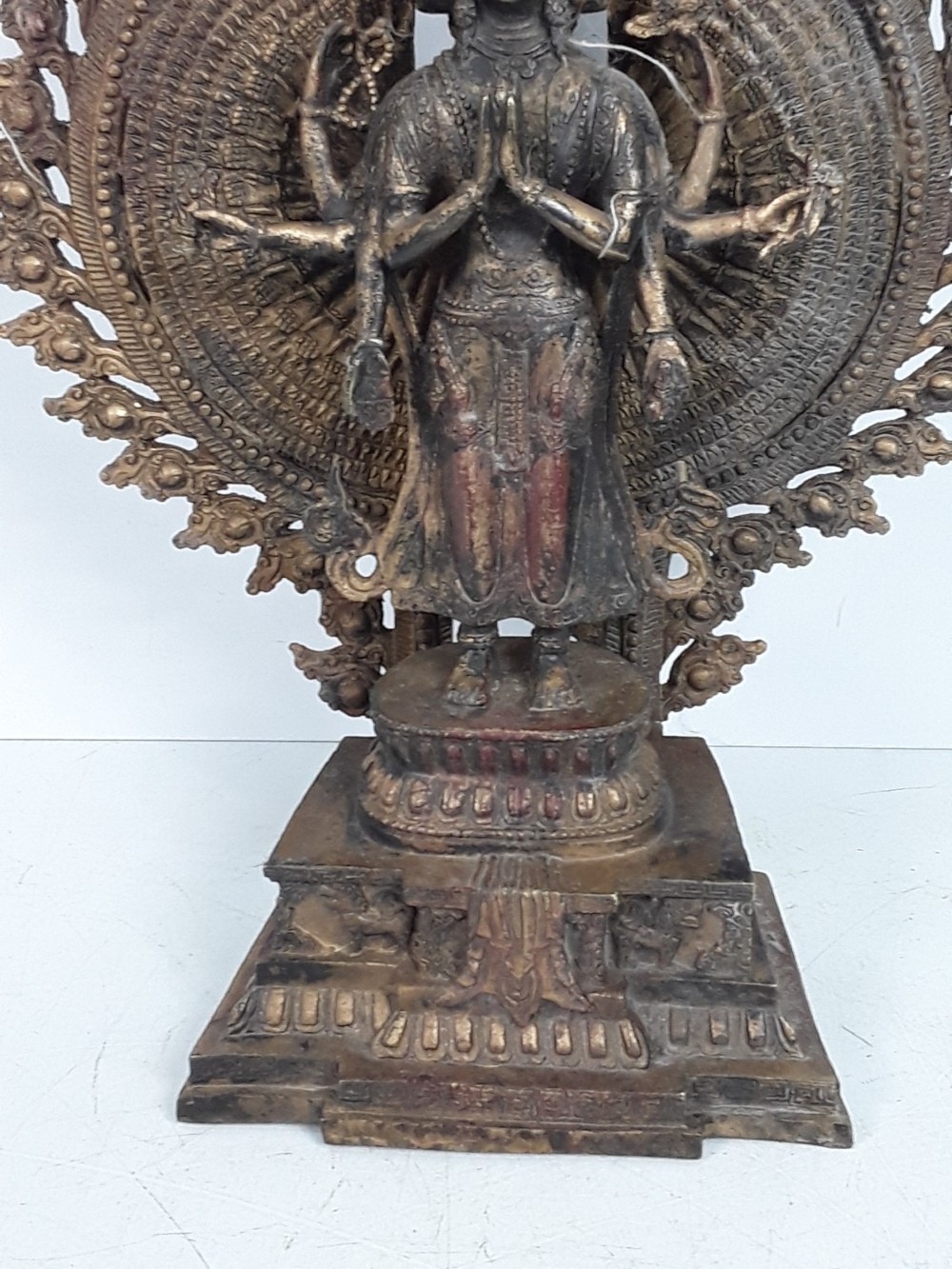 A dark bronze Tibetan sculpture depicting eleven-headed Avalokiteshvara with radiating arms set against a halo mandorla on a lotus pedestal. View III