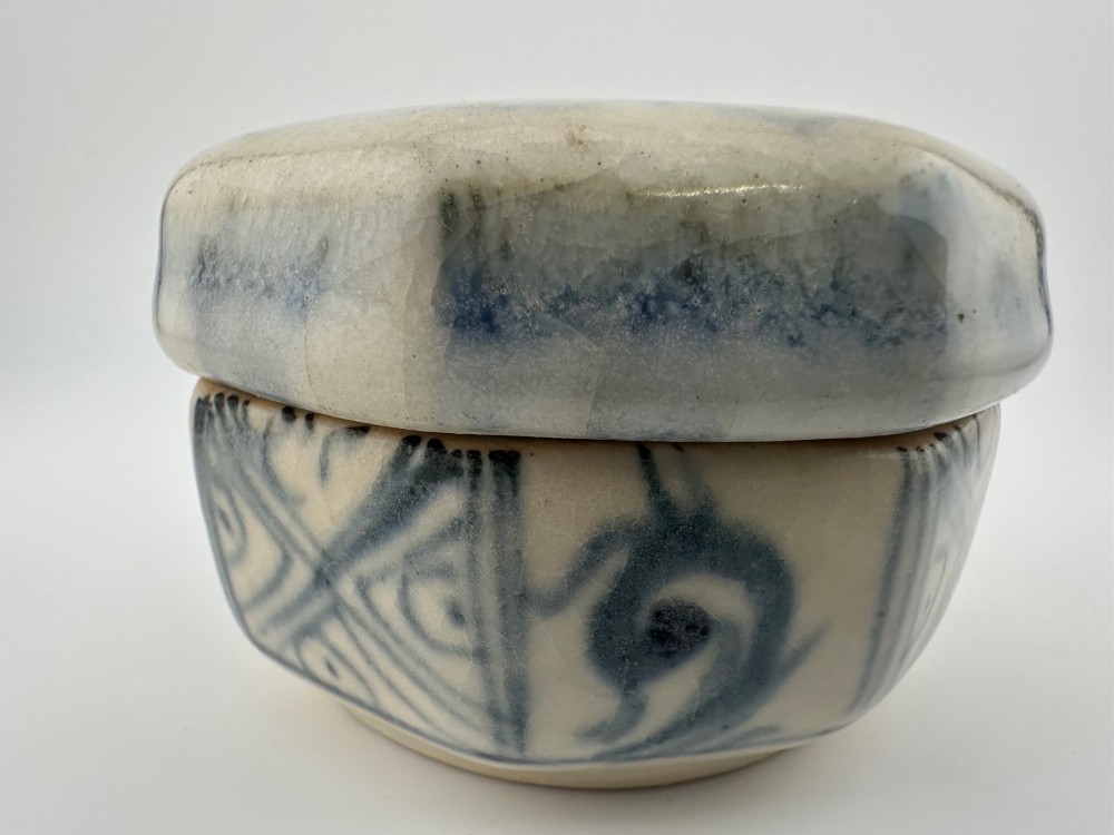 Small octagonal ceramic covered box featuring off-white glaze and hand-painted blue cobalt scroll motifs. View IX