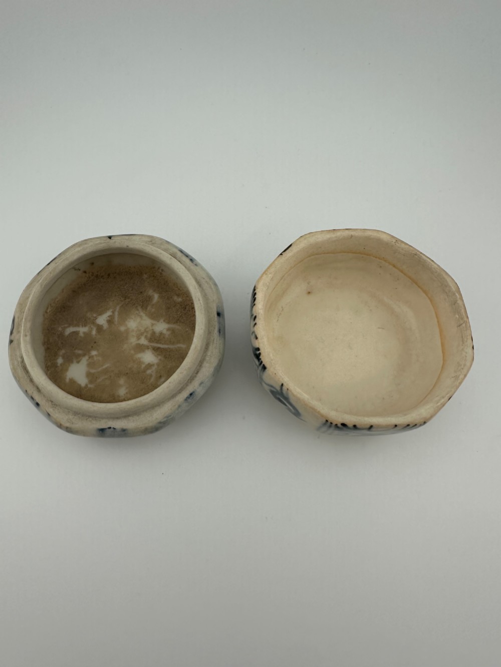 Small octagonal ceramic covered box featuring off-white glaze and hand-painted blue cobalt scroll motifs. View X