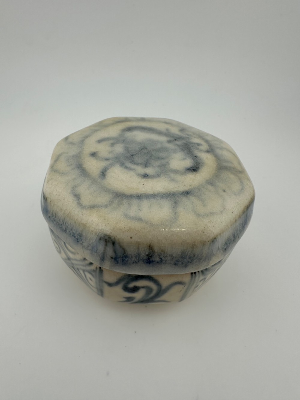 Small octagonal ceramic covered box featuring off-white glaze and hand-painted blue cobalt scroll motifs. View XI