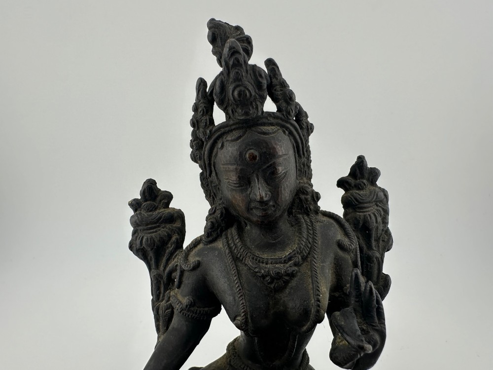 A dark bronze figure of the Buddhist deity Tara seated in lalitasana on an ornate lotus base. View IX