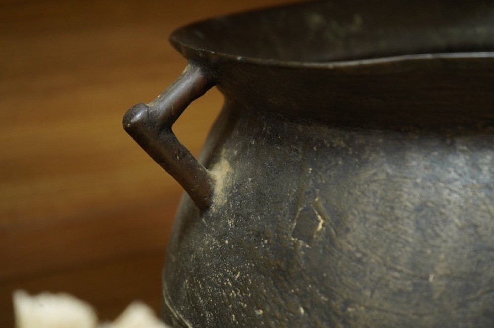 A 17th-century leaded bronze cauldron with a bulbous body, three short feet, angular side handles, and a dark patinated surface. View IV