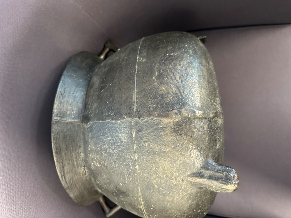 A 17th-century leaded bronze cauldron with a bulbous body, three short feet, angular side handles, and a dark patinated surface. View VI