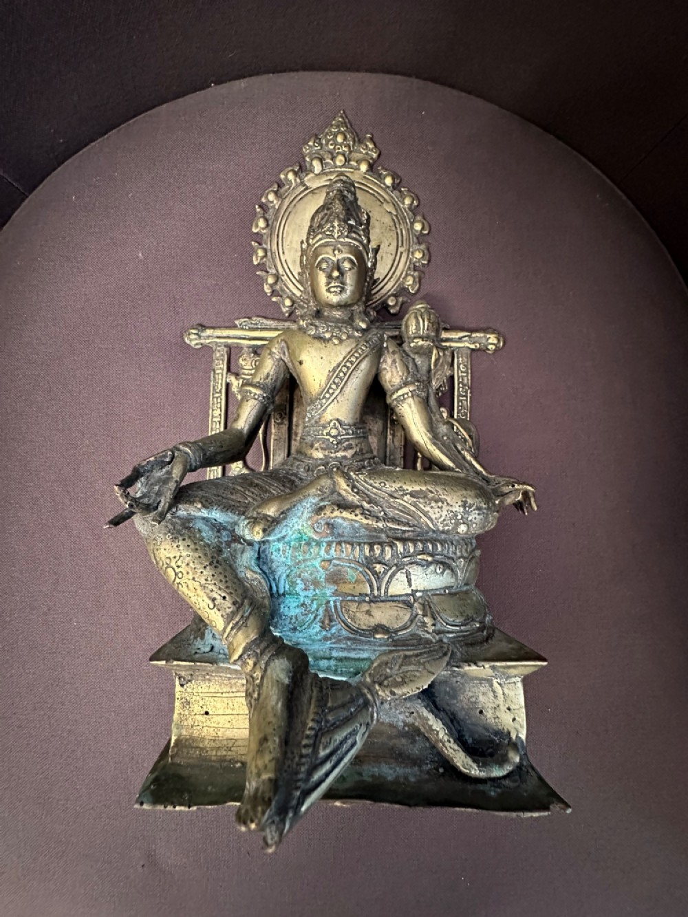 An antique cast bronze figure of Green Tara seated on an elaborate throne with a flaming halo backpiece and visible green patination. View II